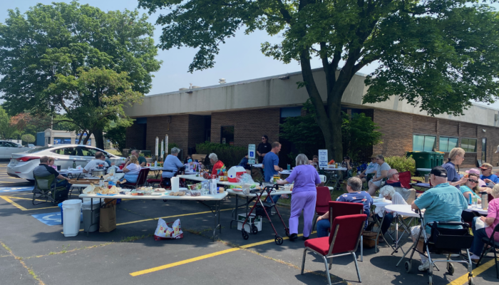 Parishioners gathering around tables outdoors with tables of food as they enjoy a pot luck in gorgeous weather celebrating the completion of the pledge drive in June 2023.